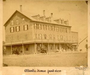 Historic sepia photograph of the Atlantic House, a large multi-story wooden hotel with wraparound porch and dormer windows, showing several people seated on the porch, photographed by McKenney of Portland, Maine.