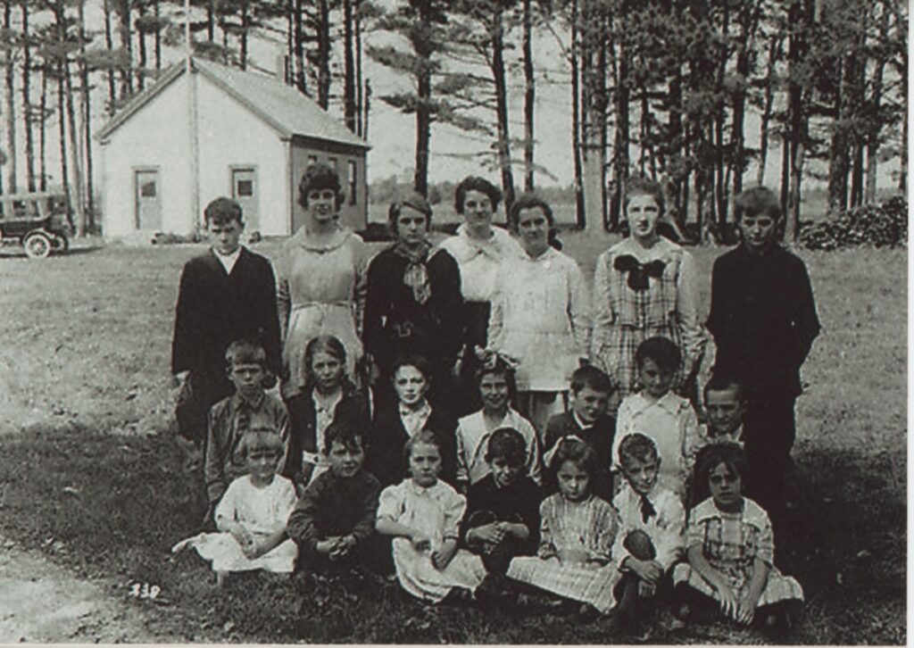 Group of students and teacher posed outside Coal Kiln Corners School in Scarborough, Maine, circa 1920, with early automobile at left.